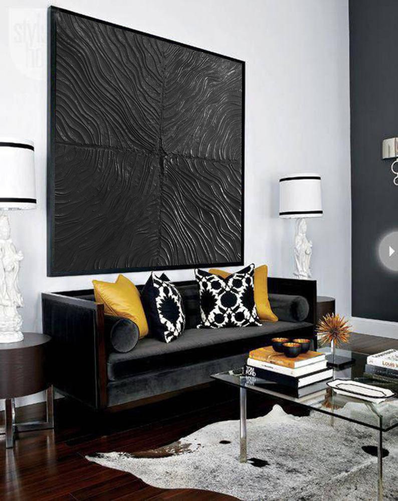 Puede incluir: Un sof&aacute; de terciopelo negro con cojines decorativos de patrones amarillos, negros y blancos se encuentra en una sala de estar moderna con una alfombra de patrones negros y blancos, una mesa de caf&eacute; de vidrio y una gran obra de arte abstracta en blanco y negro en la pared.
