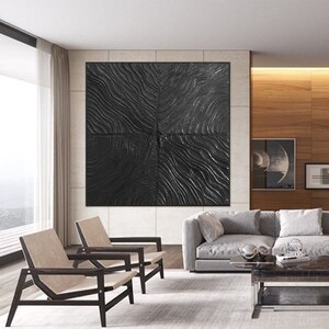 Puede incluir: Una pieza de arte de pared abstracta en blanco y negro con una superficie texturizada. El arte est&aacute; colgado en una pared en una sala de estar moderna con un sof&aacute; gris, dos sillas y una mesa de caf&eacute;.