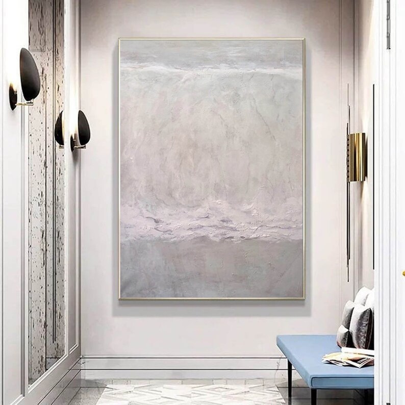 May include: Abstract painting with a light gray and white color scheme. The painting has a textured surface and a subtle horizontal line dividing the canvas. The painting is framed in a thin gold frame.