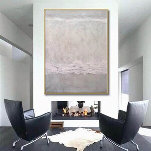 May include: Abstract painting in shades of gray and white with a textured surface. The painting is framed in a gold frame and is hanging on a white wall above a fireplace.