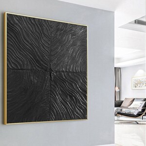 Puede incluir: Una pieza de arte de pared abstracto en negro y dorado con un patr&oacute;n texturizado y ondulado. El arte est&aacute; enmarcado en un fino marco dorado.