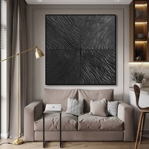 Puede incluir: Una pintura abstracta en blanco y negro con una superficie texturizada cuelga sobre un sof&aacute; beige con almohadas. La pintura est&aacute; en un marco negro y est&aacute; centrada en la pared.