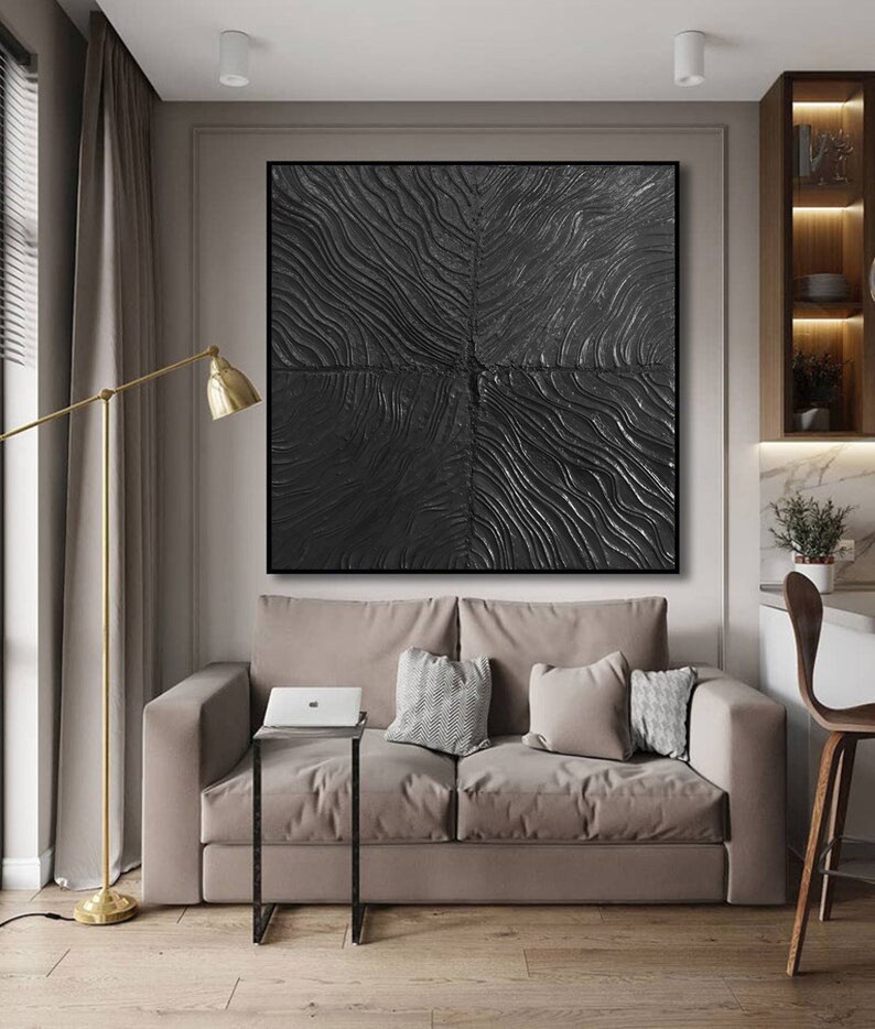 Puede incluir: Una pintura abstracta en blanco y negro con una superficie texturizada cuelga sobre un sof&aacute; beige con almohadas. La pintura est&aacute; en un marco negro y est&aacute; centrada en la pared.