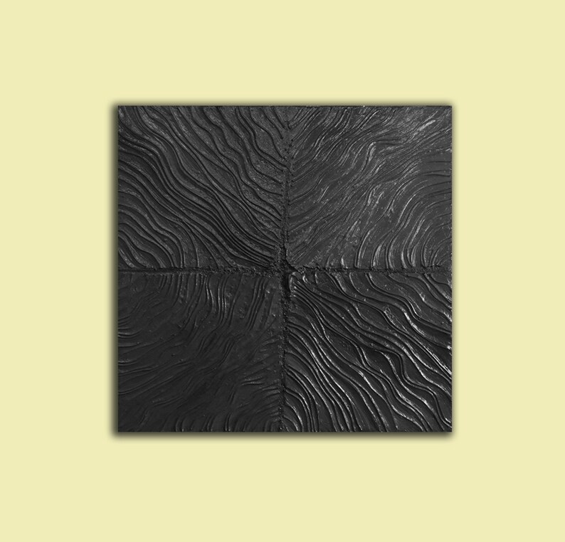 Puede incluir: Una pieza de arte de pared cuadrada negra con una superficie texturizada que se asemeja a la veta de la madera. La superficie est&aacute; dividida en cuatro secciones con una l&iacute;nea elevada en el centro de cada secci&oacute;n.