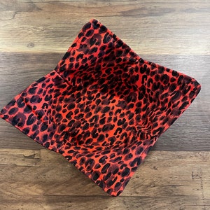 May include: A red and black leopard print fabric bowl. The bowl is made of a soft, flexible material and is perfect for holding small items.