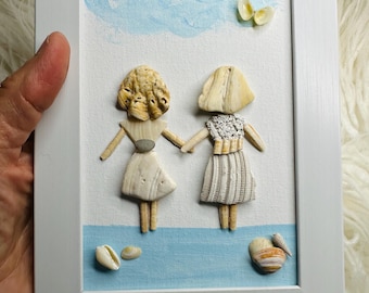 May include: A framed wall art piece featuring two figures crafted from seashells standing on a painted blue surface. The figures have shell hair and dresses, holding hands under a painted blue cloud and a small shell butterfly in a white frame.
