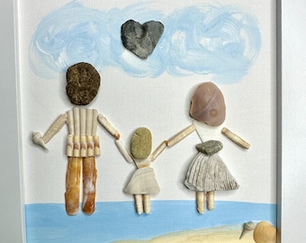 May include: A framed wall art piece featuring three figures crafted from seashells and stones on a painted background. The figures stand on a sandy beach with a blue sky and a heart-shaped stone above. The artwork is enclosed in a white frame.