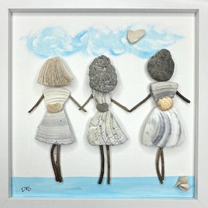 May include: A framed artwork featuring three figures crafted from seashells and stones. The figures, with shell dresses and stone heads, are holding hands against a backdrop of a blue sky with painted clouds. The artwork is signed "DMS".