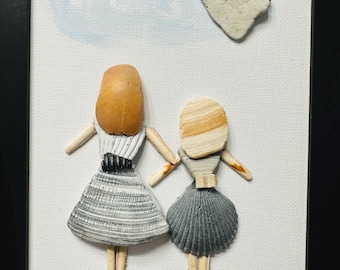 May include: A framed wall art piece featuring two figures crafted from seashells and small stones. The figures have shell hair and dresses, standing on a painted blue base. A heart-shaped stone is above them, with a starfish and shells below.