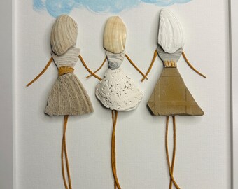 May include: A framed wall art piece featuring three figures crafted from seashells and stones. The figures have shell heads, textured shell dresses, and thin brown cord limbs. Above them is a painted blue cloud and a small shell heart.