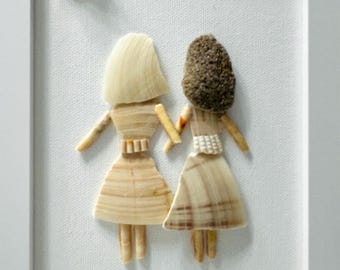 May include: A framed wall art piece featuring two figures crafted from various seashells. One figure has light-colored shell hair and a dress, while the other has dark textured shell hair and a dress. A single shell sun is positioned in the top left corner.