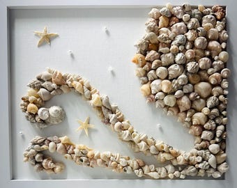 May include: A square white frame containing a wall art piece made of numerous small, light-colored seashells arranged to form a large, swirling octopus shape. Two small, light-tan starfish are attached to the white canvas background.