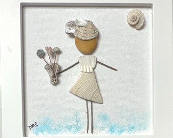 May include: A framed wall art piece featuring a figure constructed from seashells and pebbles. The figure wears a shell hat and dress, holding a shell bouquet. A spiral shell represents the sun, and blue paint accents the base. The initials DMS are visible.
