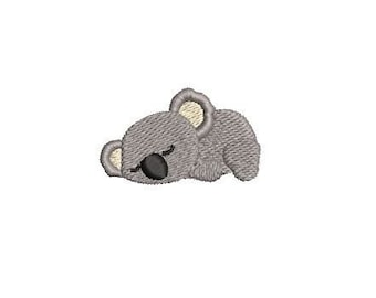 May include: A gray embroidered koala bear sleeping with its eyes closed.