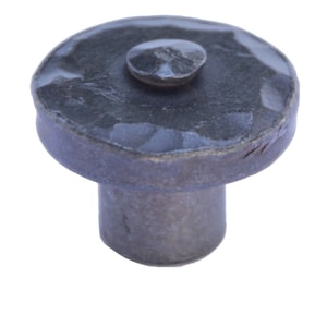 May include: A dark grey, hammered metal cabinet knob with a rounded top and a smaller, raised circular detail in the centre. The knob has a cylindrical base. The finish appears slightly textured.