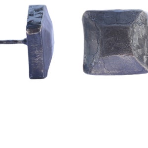 Puede incluir: Un clavo de metal negro de forma cuadrada con un acabado martillado. El clavo tiene un extremo puntiagudo y una cabeza plana.