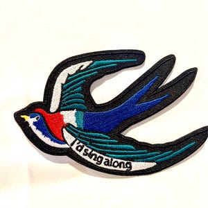 May include: Embroidered iron-on patch featuring a colorful swallow in flight with the text "I'd sing along".