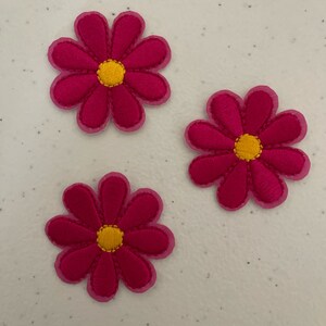 May include: Three pink fabric flowers with yellow centers. The flowers have a simple, daisy-like design.