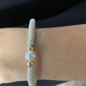 Könnte beinhalten: Ein silbernes Armband mit einer Perle und goldenen Akzenten.