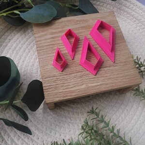 May include: Set of four pink diamond-shaped cookie cutters on a wooden surface. The cutters are different sizes.