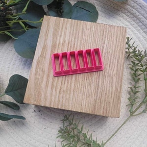 Może przedstawiać: Różowa plastikowa foremka do ciasteczek z sześcioma prostokątnymi kształtami. Foremka leży na drewnianej powierzchni.