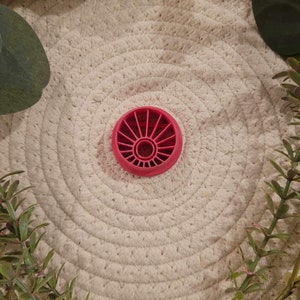 May include: A red plastic cookie cutter shaped like a sun with a circular centre and radiating lines.