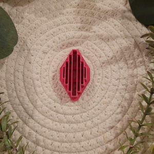 May include: A red plastic cookie cutter shaped like a diamond with vertical lines inside.