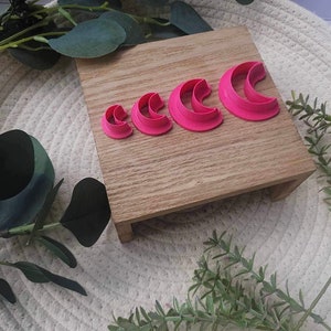 May include: A set of five pink crescent moon cookie cutters of varying sizes on a wooden surface.