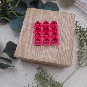 May include: A set of 12 pink cloud-shaped cookie cutters on a wooden surface.