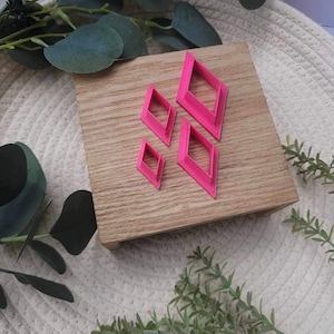 May include: Set of four pink diamond-shaped cookie cutters on a wooden surface.