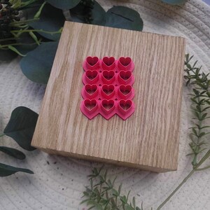 Könnte beinhalten: Ein Set aus 15 herzförmigen Ausstechern aus rosa Kunststoff auf einer Holzoberfläche.