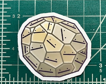 May include: A beige and brown geometric sticker with a 3D effect. The sticker has a textured surface and is shaped like a sphere.