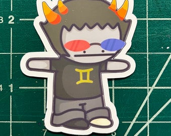 May include: A cartoon sticker of a character with brown hair, orange horns, and red and blue 3D glasses. The character is wearing a black shirt with a gold Gemini symbol. The sticker is on a green grid background.