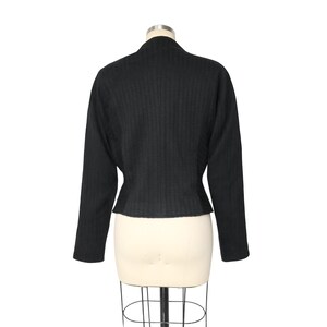 May include: Black, long-sleeved jacket with a textured, vertical stripe pattern. The jacket has a high, rounded collar and a fitted waist. The garment is displayed on a mannequin against a white background.