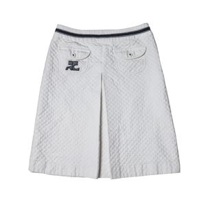 May include: A white quilted skirt featuring a diamond-patterned texture, a central front pleat, and two flap pockets at the waist. The waistband is accented with a dark navy blue striped trim, and a dark logo patch is visible on the left pocket.