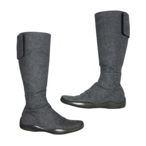 Könnte beinhalten: Zwei kniehohe Stiefel in Grau aus weichem, strukturiertem Material. Jeder Stiefel hat eine runde Spitze und eine dunkle Sohle. Oben an jedem Stiefel ist eine Klappe befestigt.