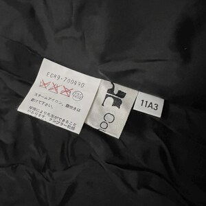 May include: Close-up of a black garment with attached tags. The tags display care symbols, the text "ECR9-700490", and the number "11A3". One tag has the word "Co" printed on it. The background is a dark, textured fabric.