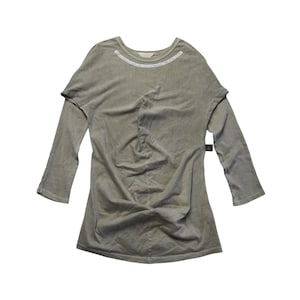 May include: A sage green long-sleeve top featuring a round neckline with white text printed along the collar, three-quarter length sleeves, and a gathered, twisted detail at the center of the hemline, creating a draped effect across the front.