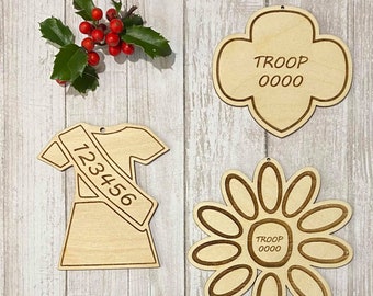 Könnte beinhalten: Drei Girl Scout-Ornamente aus Holz. Eines ist eine traditionelle Girl Scout-Kekssform mit dem Text "TROOP 0000". Ein anderes ist eine Girl Scout-Uniform mit dem Text "123456". Das letzte ist eine Blumenform mit dem Text "TROOP 0000".