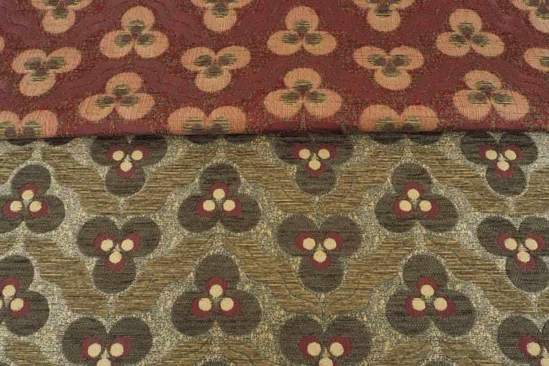 May include: Close-up of two patterned fabrics. The top fabric is a deep red with a repeating floral design in shades of peach and brown. The bottom fabric is a mix of brown, gray, and gold with a similar floral pattern in brown and red.
