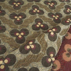 May include: Close-up of patterned fabric with a repeating floral design. The fabric features a textured background in shades of brown and gray, with dark gray floral shapes accented by burgundy and cream-colored details. A section of burgundy fabric is visible.