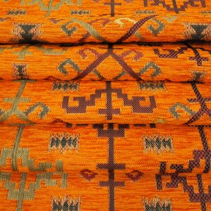 May include: Close-up of orange fabric with a woven pattern of geometric shapes in shades of brown, green, and gold.