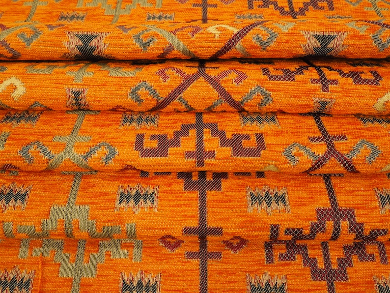 May include: Close-up of orange fabric with a woven pattern of geometric shapes in shades of brown, green, and gold.