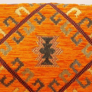 May include: Orange fabric with a geometric pattern in shades of brown, gold, and black. The pattern is woven into the fabric and creates a textured look.