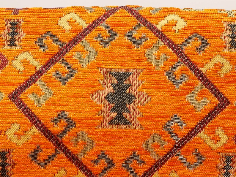 May include: Orange fabric with a geometric pattern in shades of brown, gold, and black. The pattern is woven into the fabric and creates a textured look.