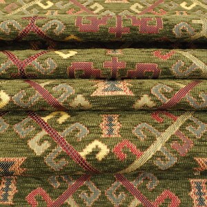 May include: Close-up of a green fabric with a woven pattern of red, gold, and blue geometric shapes. The fabric is folded in layers, showing the intricate details of the design.