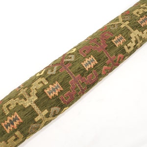May include: A green, red, and gold patterned fabric with a geometric design. The fabric is woven with a textured surface.