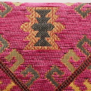 May include: Pink and gold patterned throw pillow with a geometric design. The pillow has a soft, textured fabric.