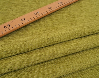 May include: Close-up of a green textured fabric with a wooden ruler on top. The ruler is marked with numbers from 0 to 60.