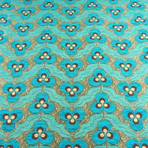 May include: Close-up of a patterned fabric with a repeating floral design. The flowers are turquoise with brown and cream-colored centers, set against a silver-gray background. The fabric has a textured appearance, with a wavy turquoise pattern.
